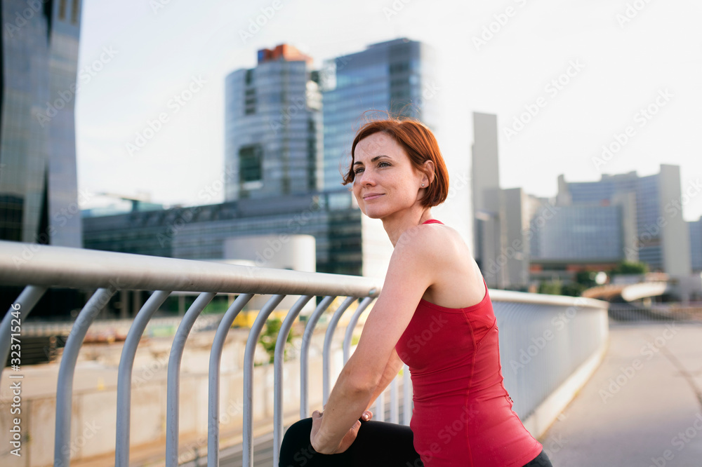 Young woman runner with earphones in city, stretching.