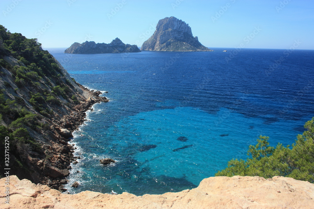 The island of Es Vedra between the blue sky and the blue sea of ​​the Ibizan coasts in front of the Cala D'Hort beach in the Balearic Islands
