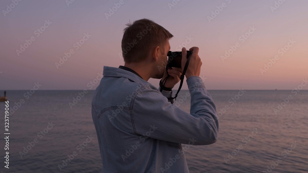 A photographer's man in a denim shirt takes photos of the sea at sunset. A photographer's man in a denim shirt takes photos of the sea at sunset.