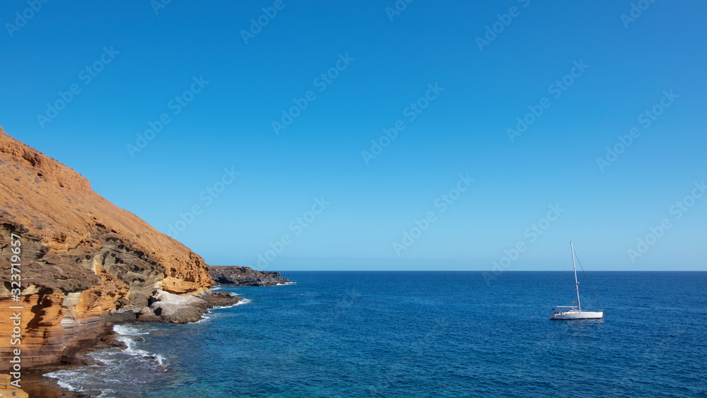 Cozy secluded bay with a floating yacht near the colorful eroded volcanic cone known as Montana Amarilla, Costa del Silencio, Tenerife, Canary Islands, Spain Cozy secluded bay with a floating yacht near the colorful eroded volcanic cone known as Montana Amarilla, Costa del Silencio, Tenerife, Canary Islands, Spain
