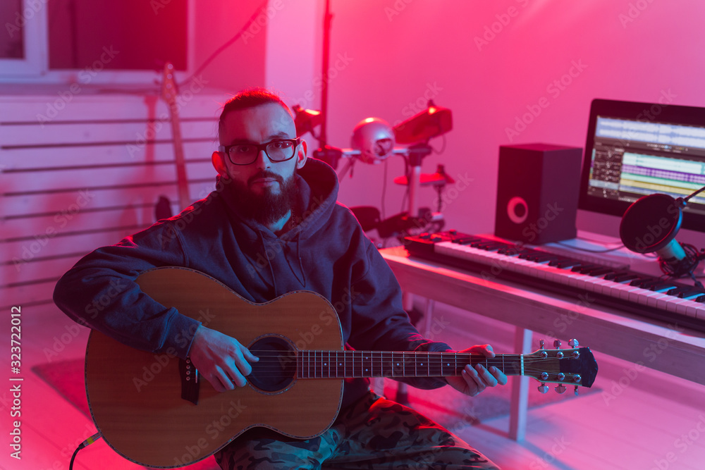 Fototapeta Create music and a recording studio concept - Bearded man guitarist recording electric guitar track in home studio