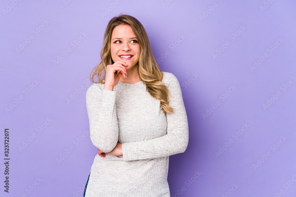 Young caucasian woman isolated on purple background relaxed thinking about something looking at a copy space. Young caucasian woman isolated on purple background relaxed thinking about something looking at a copy space.