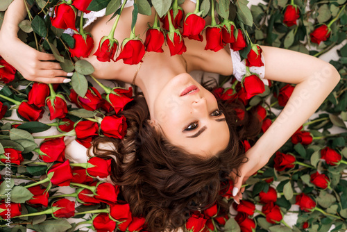 Close-up portrait of a beautiful brunette woman in roses. The girl lies surro...