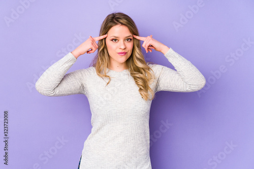 Young caucasian woman isolated on purple background focused on a task, keeping forefingers pointing head.