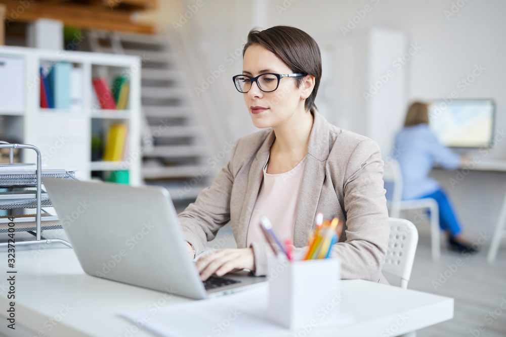 Portrait of successful businesswoman using laptop while working in modern white office, copy space