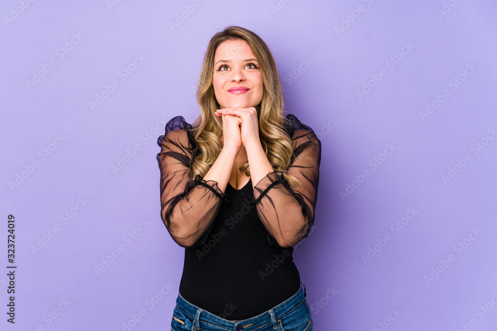 Young caucasian woman isolated on purple background keeps hands under chin, is looking happily aside. Young caucasian woman isolated on purple background keeps hands under chin, is looking happily aside.