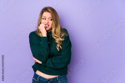 Young caucasian woman isolated on purple background biting fingernails, nervous and very anxious.