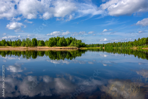 Finland, Lapland, Ivalo: Panorama view of pure rural Finnish nature with calm lake water, cloud reflections, green trees, riverbank and blue sky in background - concept remote rural nobody environment