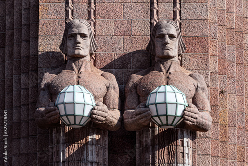 Republic of Finland, Helsinki: Fragment of famous Helsinki Central Station main railway station facade in the Finnish capital with sculptures statues holding spherical art nouveau lamps.