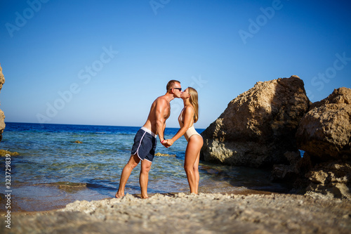a guy in shorts and a girl in a swimsuit cuddling against the blue water of the red sea