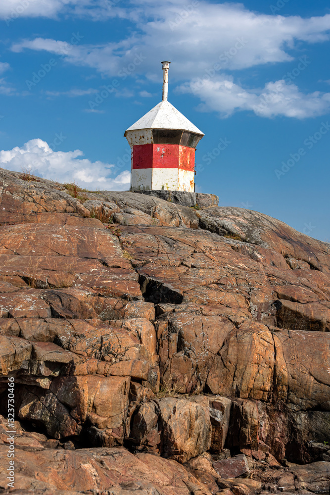Republic of Finland, Helsinki, Suomenlinna: Abandoned beautiful red white striped lighthouse on rocky cliff from below with blue sky in the background - concept nautical danger navigation travel