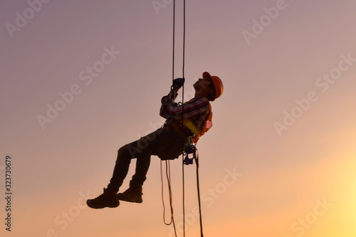 Construction worker wearing safety work at high uniform on scaffolding at construction site on during sunset,Working at height equipment. © saravut