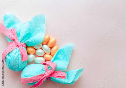 Egg gift in green paper packaging and with pink ribbon Easter Bunny wrap idea. Chocolate dragee white and gold color, multicolor colorful feathers. Minimal concept. Flat lay, Copy space, top view