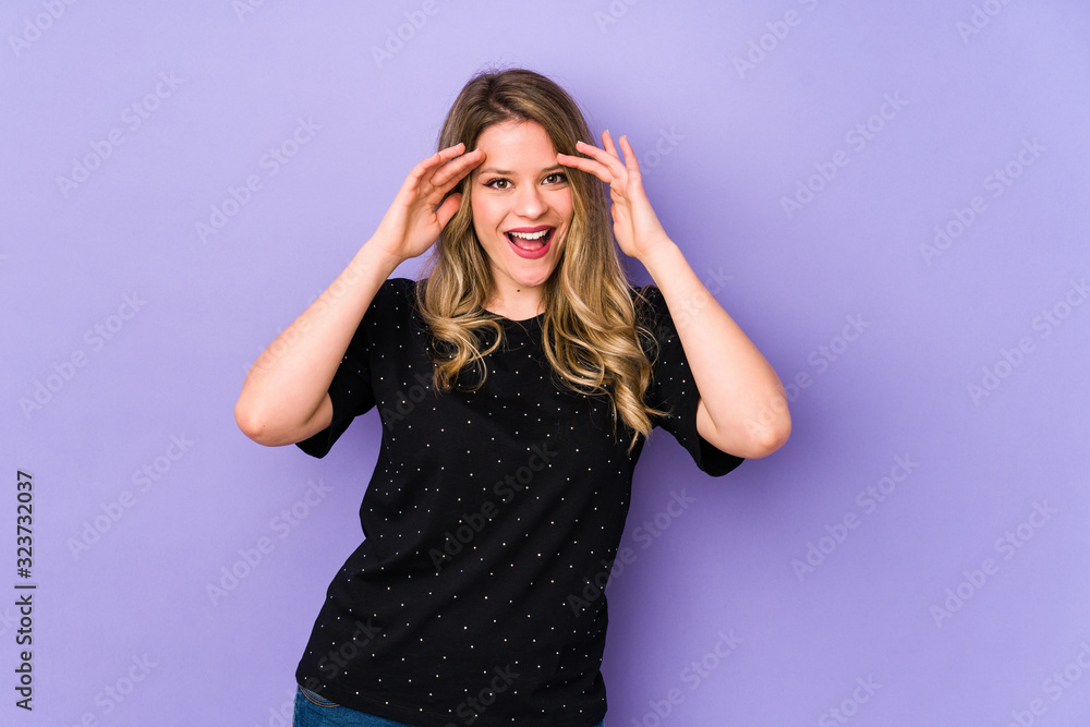 Naklejka premium Young caucasian woman isolated on purple background receiving a pleasant surprise, excited and raising hands.