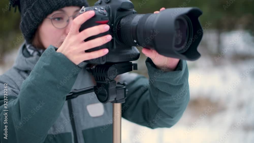 The girl enthusiastically takes pictures in the winter forest on a photo camera, which is standing on a tripod The girl enthusiastically takes pictures in the winter forest on a photo camera, which is standing on a tripod