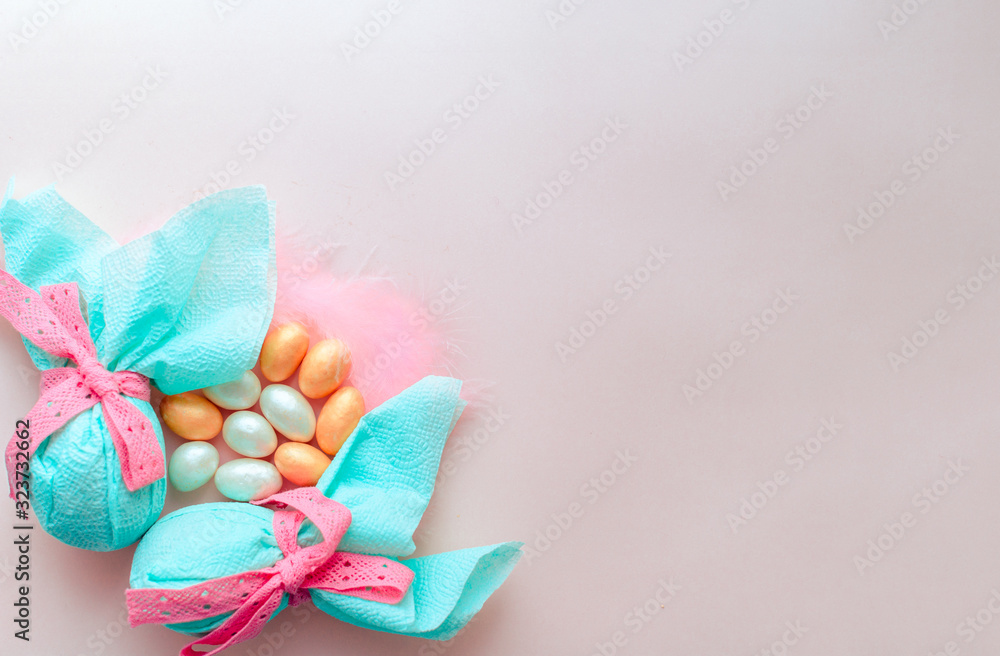 Egg gift in green paper packaging and with pink ribbon Easter Bunny wrap idea. Chocolate dragee white and gold color, multicolor colorful feathers. Minimal concept. Flat lay, Copy space, top view