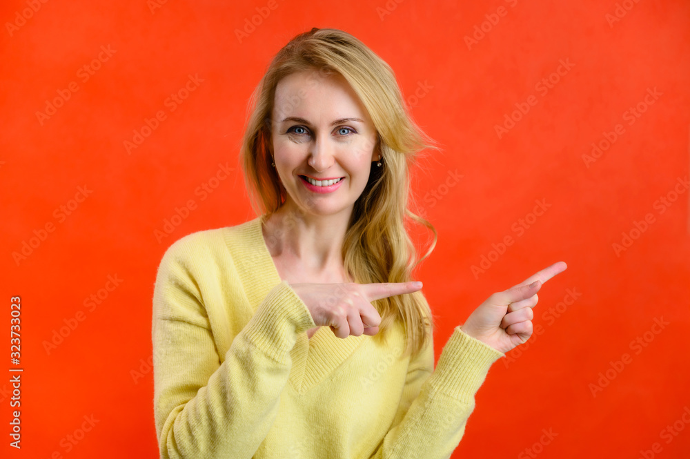 Obraz premium Photo of a 40-year-old blonde woman in a yellow sweater showing her fingers on a red background
