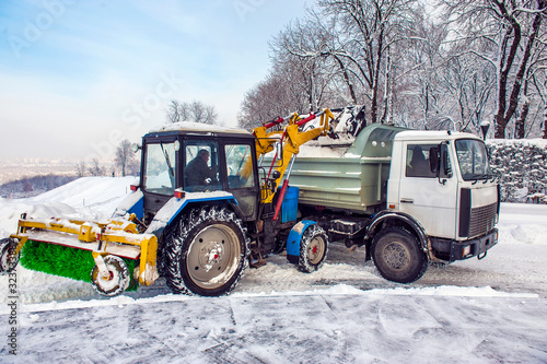 Snow cleaning tractor snow-removal machine loading pile of snow on a dump truck.