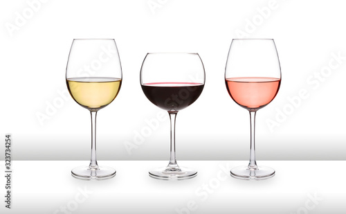 Three glasses of wine, white, red and rose, on a white bar like surface, with a white background and graduated tint