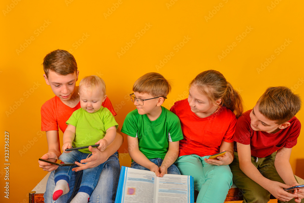 A small child sits with a smartphone, the rest of the children look at him. A small child sits with a smartphone, the rest of the children look at him.