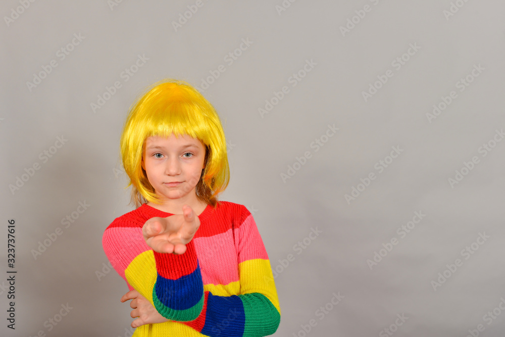 A girl in a yellow wig points to a place for an advertising product, a bright colored child on a gray background. A girl in a yellow wig points to a place for an advertising product, a bright colored child on a gray background.