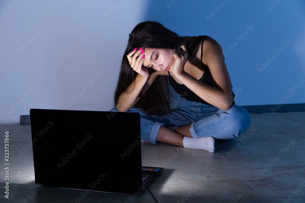 sad and female teenager with tablet computer and laptop suffering cyberbullying and harassment being online abused by stalker or gossip feeling desperate and humiliated in cyber bullying