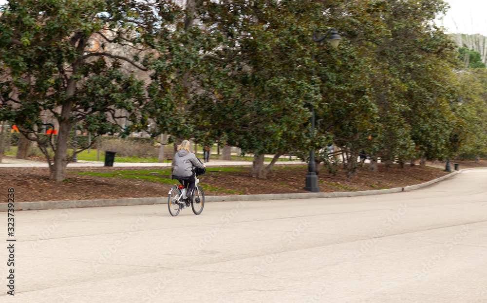 middle-aged woman with blond hair, walks or bike through paved park
