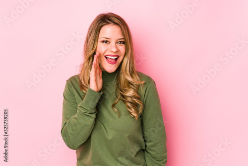 Young caucasian woman isolated on pink background shouts loud, keeps eyes opened and hands tense.