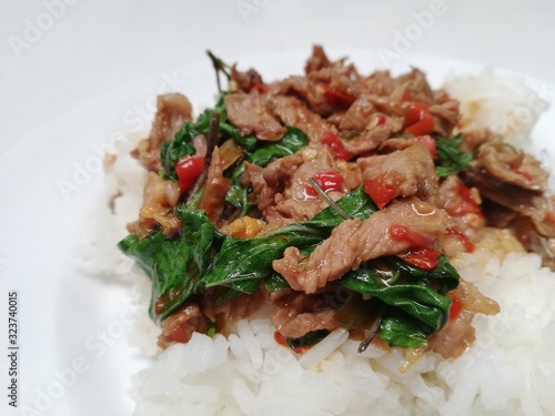 Popular spicy Thai dish, jasmin rice topped with stir fried beef with basil leaves, chilli and garic on white plate. photo