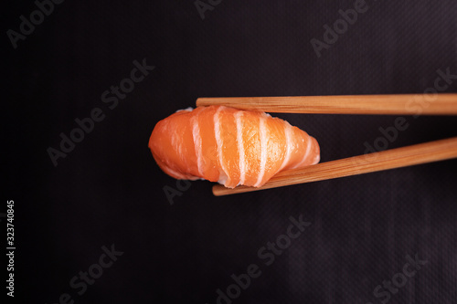 Stock photo of sushi Nigiri grabbed by chopsticks on a black background.