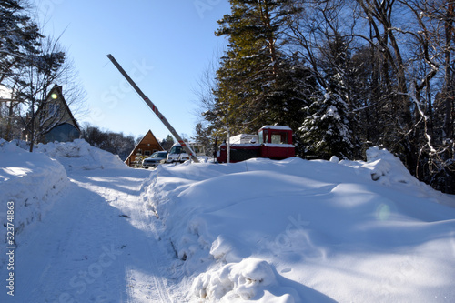 A snow-covered terrain, snow and forest, and in the distance a barrier is visible, behind it is a large tractor in the snow and several cars of the guests of the camp site. Winter landscape,