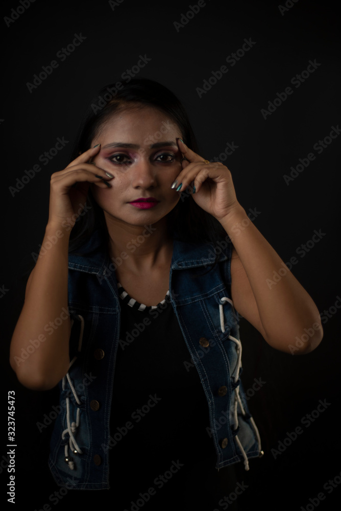 Fashion portrait of an young and attractive Indian Bengali brunette girl with tee shirt and blue western jacket tying hair in front of a black studio background. Indian fashion portrait and lifestyle. Fashion portrait of an young and attractive Indian Bengali brunette girl with tee shirt and blue western jacket tying hair in front of a black studio background. Indian fashion portrait and lifestyle.