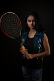 Fashion portrait of an young and attractive Indian Bengali brunette girl with tee shirt, blue western jacket and racket in front of a black studio background. Indian fashion portrait and lifestyle.