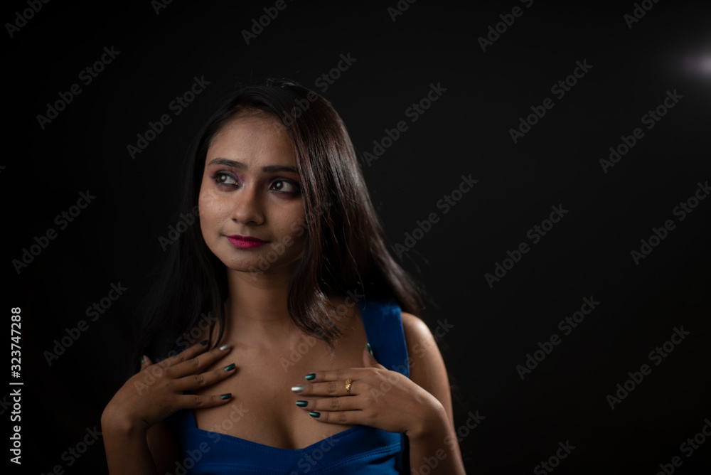 Naklejka premium Fashion portrait of an young and attractive Indian Bengali brunette girl with blue western dress in front of a black studio background. Indian fashion portrait and lifestyle.