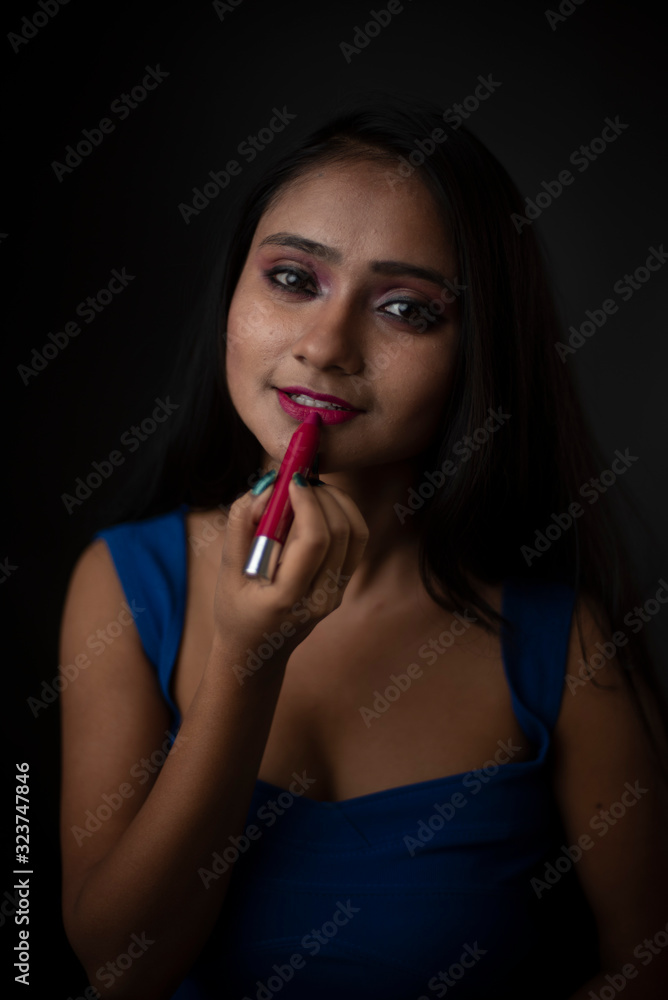 Fashion portrait of an young and attractive Indian Bengali brunette girl with blue western dress doing make up in front of a black studio background. Indian fashion portrait and lifestyle. Fashion portrait of an young and attractive Indian Bengali brunette girl with blue western dress doing make up in front of a black studio background. Indian fashion portrait and lifestyle.
