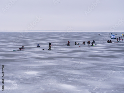 large number of people and tents on ice of reservoir gathered on sunny winter day to do winter fishing. Hobby concept