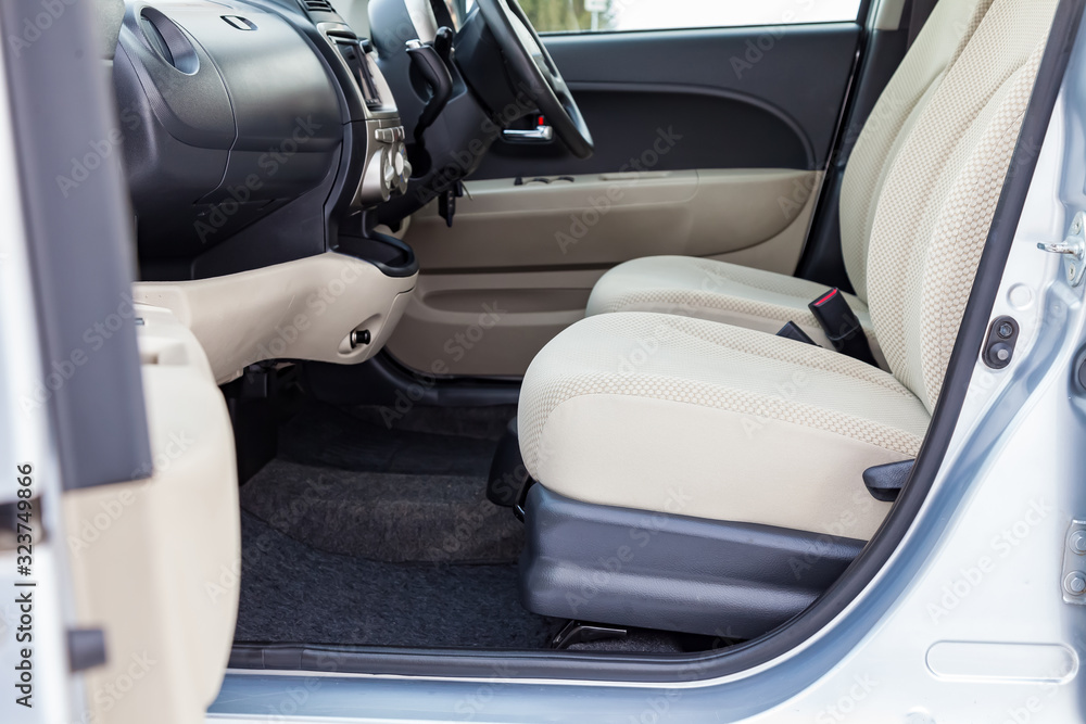 Comfortable front seats inside the car: the driver and passenger, tied with beige velourus, modern interior design, the steering wheel covered and a luxurious center console.