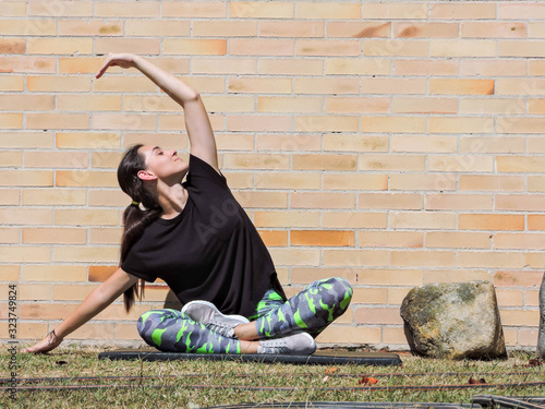 Mujer joven haciendo yoga con camisa negra y fondo de ladrillo