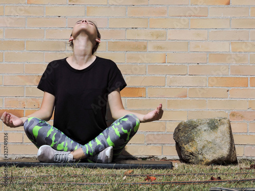 Mujer joven haciendo yoga con camisa negra y fondo de ladrillo