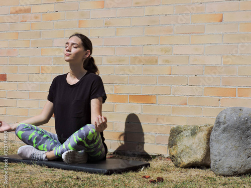Mujer joven haciendo yoga con camisa negra y fondo de ladrillo