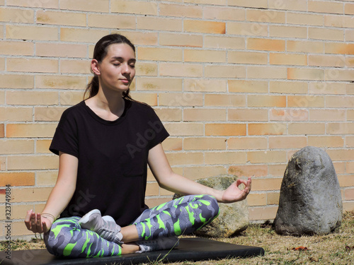 Mujer joven haciendo yoga con camisa negra y fondo de ladrillo