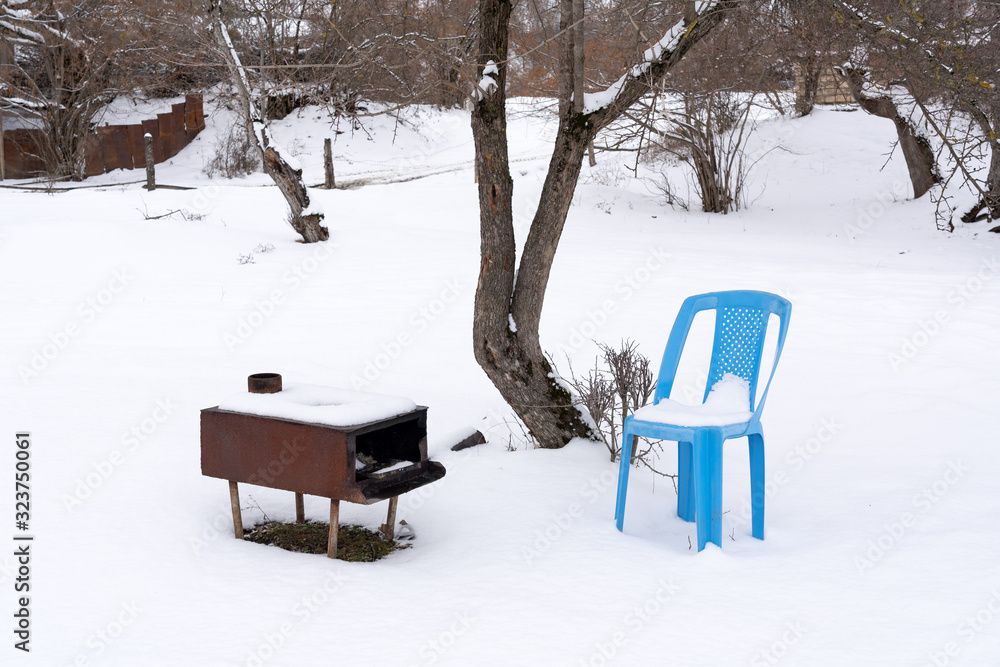 Metal outdoor oven and plastic chair in a snowy patio