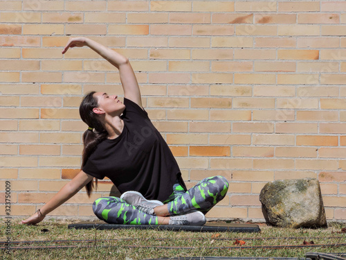 Mujer joven haciendo yoga con camisa negra y fondo de ladrillo