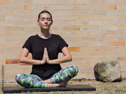 Mujer joven haciendo yoga con camisa negra y fondo de ladrillo