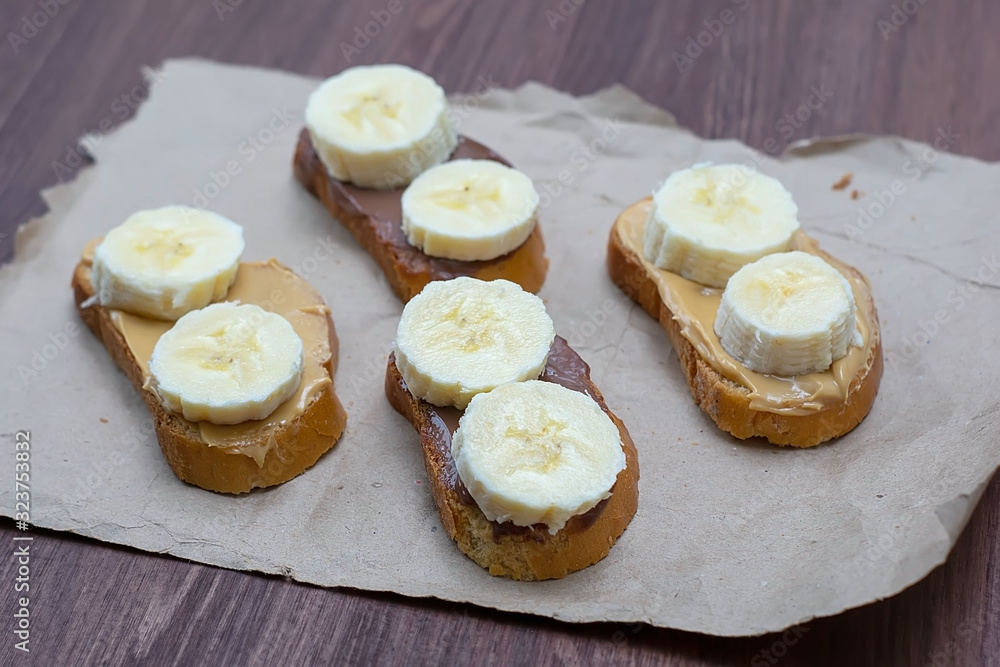 Sandwiches with peanut butter and chocolate paste with banana slices on a dark background. Home Fast Food Concept Sandwiches with peanut butter and chocolate paste with banana slices on a dark background. Home Fast Food Concept
