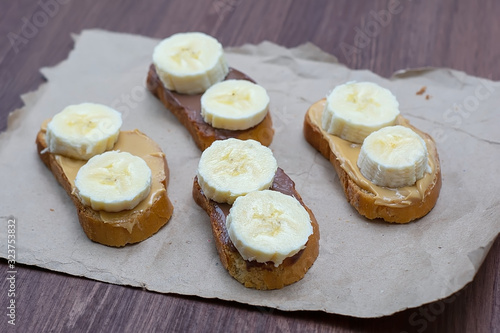 Sandwiches with peanut butter and chocolate paste with banana slices on a dark background. Home Fast Food Concept