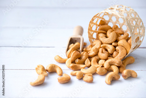 Roasted tasty cashew nuts in wooden spoon in bowl on a white  wooden table, isolated background with copyspace for your text.