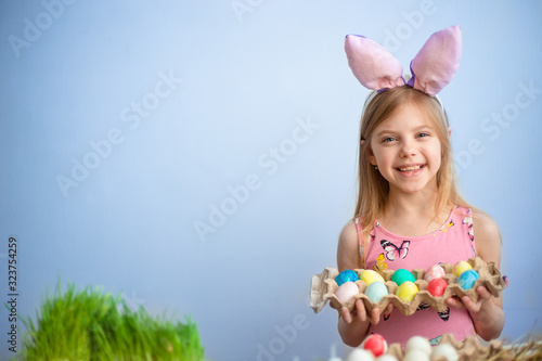 Cute little baby wears bunny ears on Easter day. cute little girl holding a package of Easter painted eggs