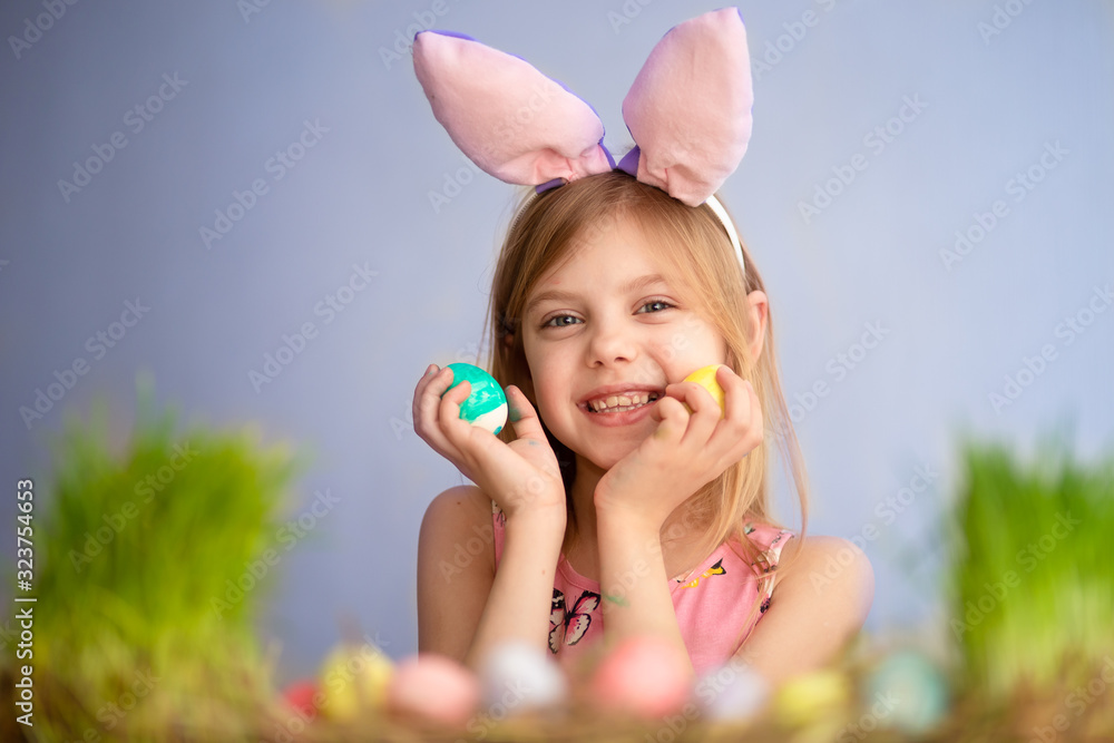 Cute little baby wears bunny ears on Easter day. cute little girl holding easter eggs in her hands and smiling. blue background Cute little baby wears bunny ears on Easter day. cute little girl holding easter eggs in her hands and smiling. blue background