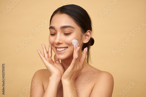 Young girl smiles and puts cream on her face on a yellow background